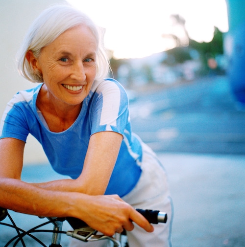 Portrait of an elderly woman smiling leaning forward on bicycle handlebars